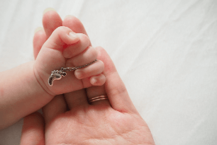 ネックレスを握る赤ちゃんの手を優しく包み込むお母さんの手の写真